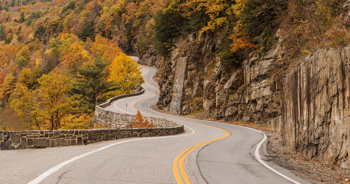 Curvy mountain road with vibrant fall foliage in New York's forested landscape.