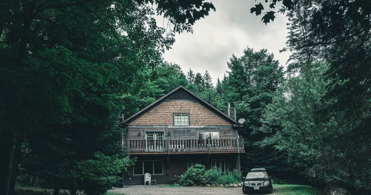 Beautiful wooden house nestled in Mont-Tremblant forest with parked car and lush greenery.