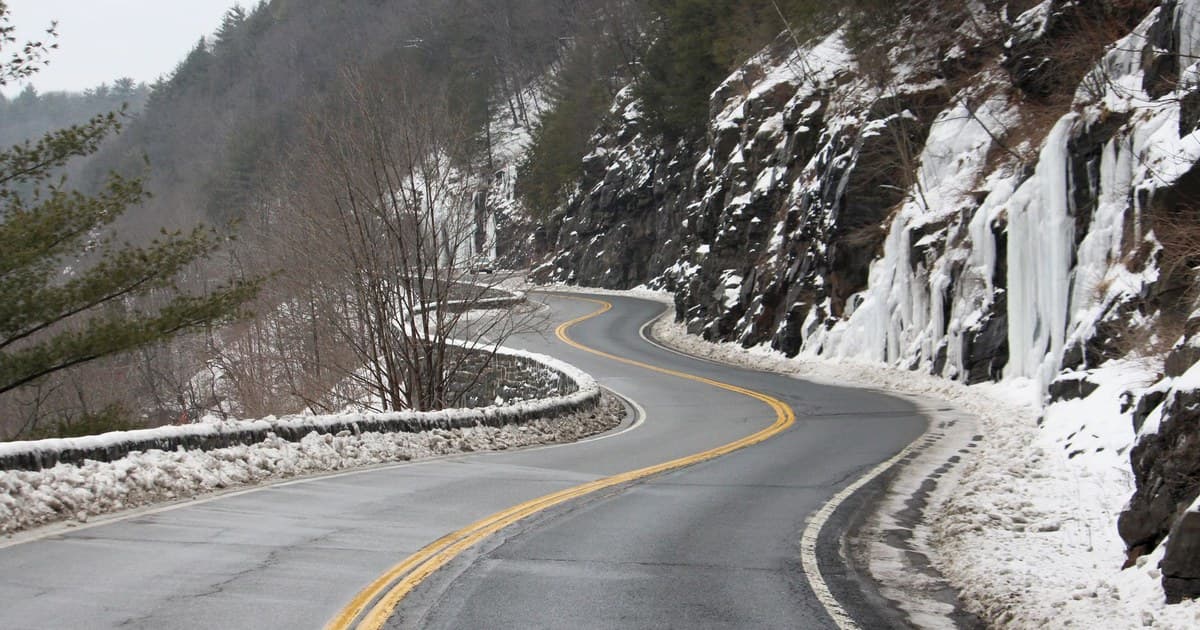 A scenic drive along a winding mountain road with snow and ice formations in winter.